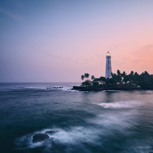 Illuminated lighthouse in the middle of palm trees. South coast of Sri Lanka at sunset.